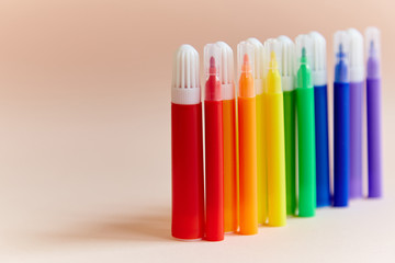 Colored markers thin thick red yellow green pink blue purple light background. Office supplies rainbow color are on the table on the righ