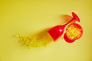 One red glass stands on a table with a yellow background. One glass is down. There is a yellow paper drink in the glass .