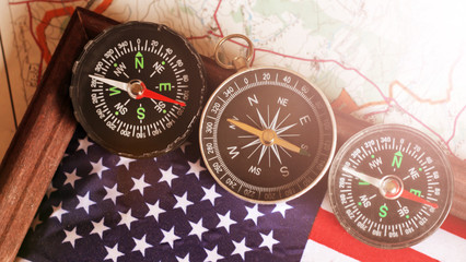 Three compasses and an American flag in a wooden frame, travel theme, top view