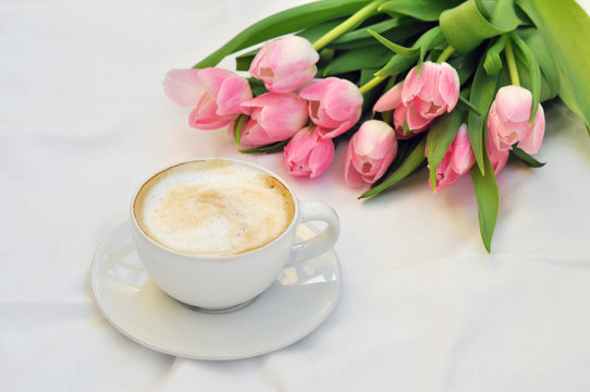 cup of coffee and bouquet of tulips on white background