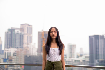 Fototapeta na wymiar Young beautiful Asian tourist woman against view of the city