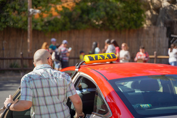 Picture of young man in cap and plaid shirt sitting in back seat in yellow taxi. Happy male getting into a cab. Businessman entering a taxi on city street