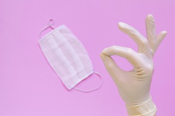 Protective face mask or medical mask in hand protected by white gloves on pink background. Coronavirus disease,Concept of health and medicine, virus prevention.