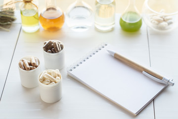 Various capsules with dietary supplements, ingredients for their creation and a notebook with a pen