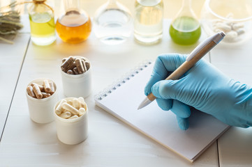Dietary supplement capsules. Hand of a pharmacist writes in a notebook