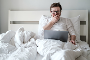 Man with a laptop in bed received bad news, he is scared and upset. Concept of remote work during quarantine.