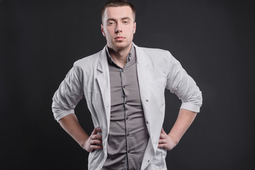 Obraz premium Young, pretty man in a medical coat on a gray background. The concept of medical education and medical activity