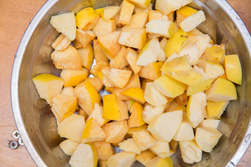 standing on a wooden chopping board . Quince fruit is cut into large pieces, composed in metallic heat resistant pot, bake,