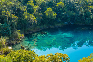 Fototapeta na wymiar View of the Cenote of Candelaria in Huehuetenango, Guatemala, on a sunny day where you can see the turquoise color of the water and the reflection of the trees in the water.