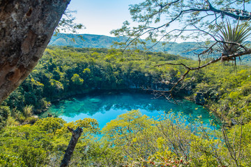 View of the Cenote of Candelaria in Huehuetenango, Guatemala, on a sunny day where you can see the turquoise color of the water and the reflection of the trees in the water.