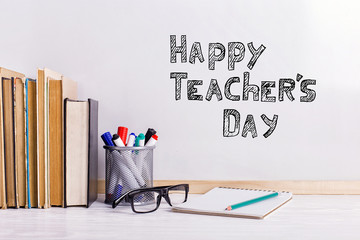 The inscription marker on a white board, Happy Teacher's Day. A table with books, glasses and attributes for writing.