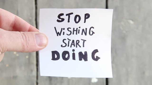 stop wishing start doing. Hand holds a piece of paper with the inscription.
