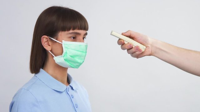 young woman in respiratory protection mask looking to side and doctor arm measure her body temperature with electro termometr