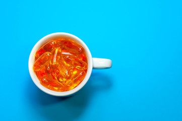 White mug with pills capsules on a blue background with copy space top view. Medicine, virus treatment, coronavirus, epidemic