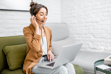 Young business woman working on computer, talking online using a headset while sitting on the...