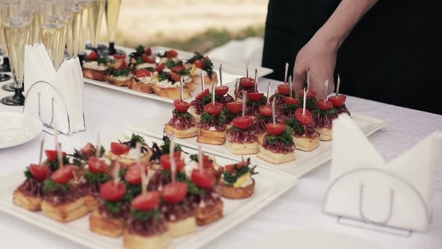 Crop stock video of an anonymous woman putting canape or sandwiches with vegetables and sausages on wedding table. Unrecognizable waitress serving the reception at banquet.