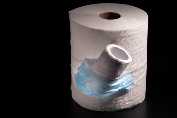 Large and small roll of toilet paper or paper towels with a medical mask on a black background