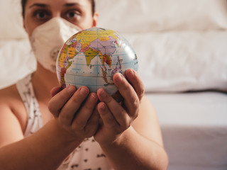 white woman using protection mask holds a small globe with both hands