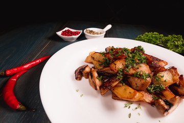 A plate of appetizing potato with mushrooms on a wooden table, among seasonings. Studio photography of food in the cooking industry, dark background.