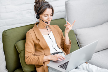 Young business woman working on computer, talking online using a headset while sitting on the...