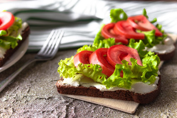 Sandwiches. Rye bread with cream cheese, tomatoes and lettuce on the wooden board and linen towel on cement background. Healthy snack. Breakfast