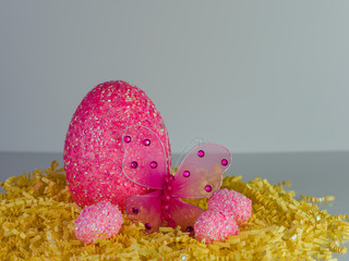 Large pink beaded Easter egg on a bed of yellow paper shreds with a pink mesh butterfly with...