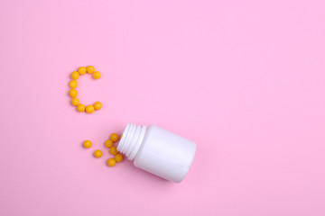 vitamins are scattered on a pink background like the letter C