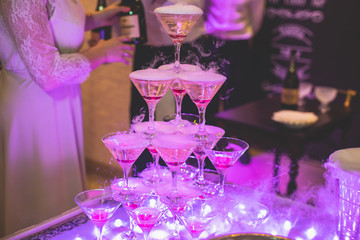 Glasses with alcoholic beverages in the pyramid, beautiful pyramid line of different colored alcohol cocktails with champagne on a wedding party, catering banquet table