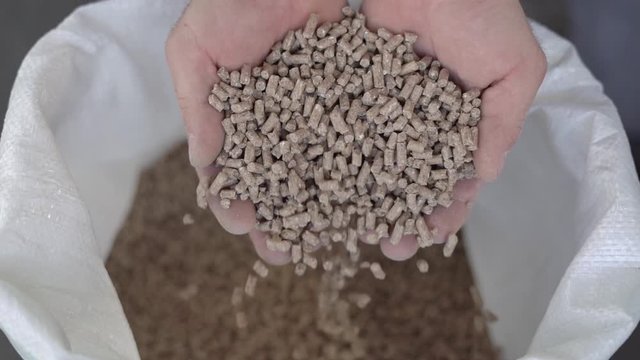 Granule feed for rural animals falls from the hands of a male farmer. Slow motion