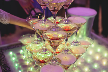 Glasses with alcoholic beverages in the pyramid, beautiful pyramid line of different colored alcohol cocktails with champagne on a wedding party, catering banquet table