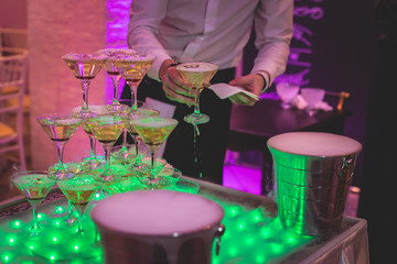 Glasses with alcoholic beverages in the pyramid, beautiful pyramid line of different colored alcohol cocktails with champagne on a wedding party, catering banquet table