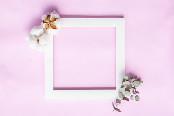 Creative composition - square frame, fresh eucalyptus leaves and cotton flowers on light pink background. Delicate floral background. Flat lay, top view, copy space