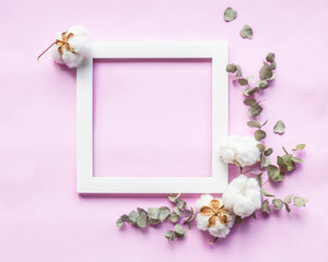 Creative composition - square frame, fresh eucalyptus leaves and cotton flowers on light pink background. Delicate floral background. Flat lay, top view, copy space