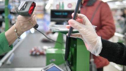 A woman at the checkout in a supermarket gives a customer a card with a laser from her smartphone. Paying in the supermarket in protective gloves so as not to get coronavirus
