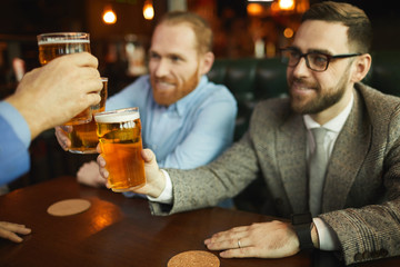 Group of men toasting with glasses of beer while have a meeting in cafe and resting after work