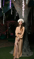 spring girl in a beige dress and a flower wreath on her head among the trees