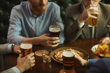Close-up of young people sitting at the table drinking beer and eating peanuts in the bar