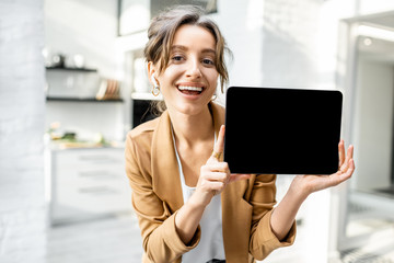 Well-dressed cheerful business woman with a digital tablet indoors, showing tablet with a black...