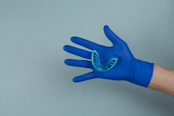 myofunctional trainer for correction of bite and alignment of teeth in the hand of doctor in the glove  on blue background