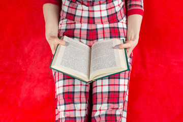 a woman in red checked home suite with a book at home on a red background in quarantine coronavirus