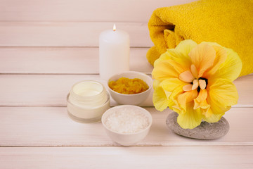 spa composition with hibiscus flower, towel, sea salt and body scrub on a white wooden background. Copy space