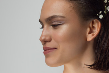 Naklejka premium Close up portrait of a face with beautiful skin and nude makeup, eyeliner and long eyelashes, puffy natural lips and white flowers. Fashion photography. Cosmetology and spa. Freshness of spring