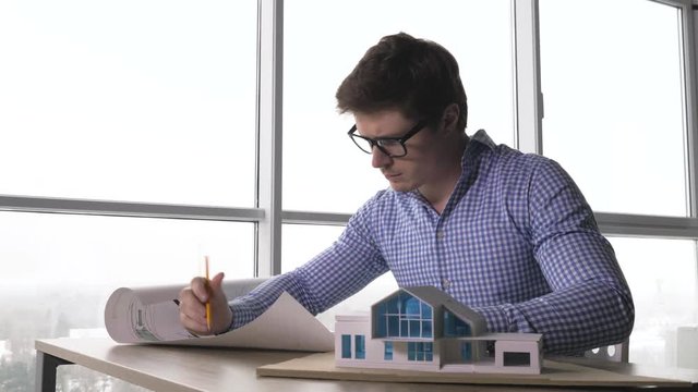 young male architect examing house plan and house model