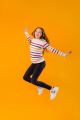 young girl teen model poses on a yellow background in a multi-colored striped jacket. Emotions, space for text