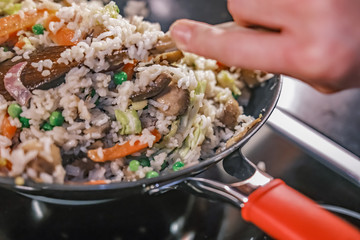  Unidentifiable chef stirring a rice, carrot, green pea and mush dinner cooking in a non-stick wok on the hob