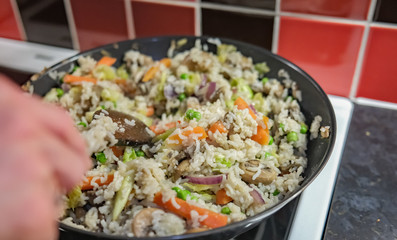  Unidentifiable chef stirring a rice, carrot, green pea and mush dinner cooking in a non-stick wok on the hob