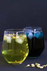 Iced butterfly pea tea and Jasmine tea. two glass of cold tea with dry flowers on a black table. Healthy lifestyle. glass of blue and yellow herbal cocktail on a black background.