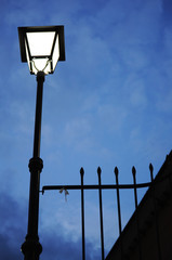 silhouette of Spanish streetlight next to metal bars in night time on a cloudy day