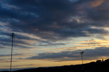 Cloudy sunset over a town with silhouettes of two television antennas.