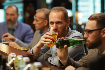 Young man enjoying the glass of beer while sitting at the bar counter together with his friends